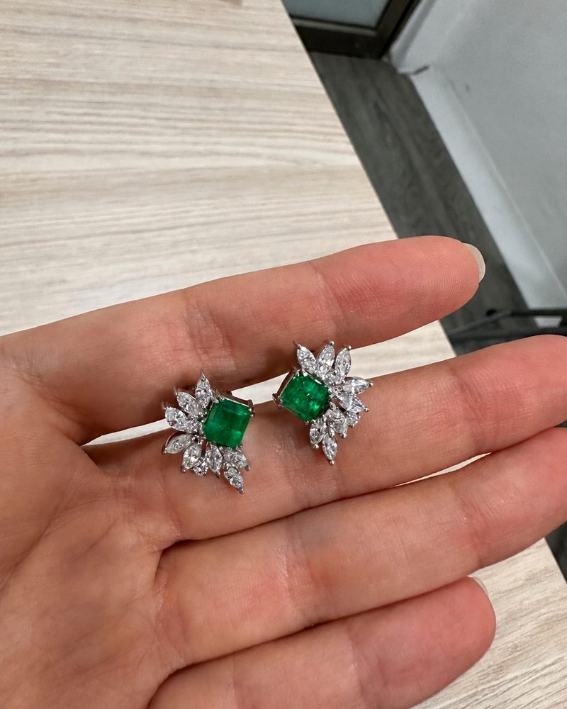 Emerald and diamond earrings held in the palm of a hand